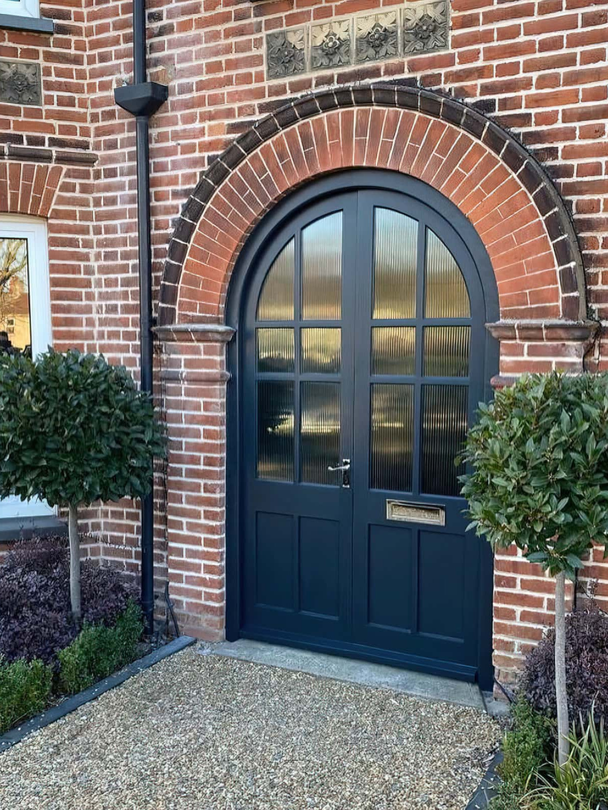 A brick house with a blue door and a tree in front of it, featuring a bespoke front door.
