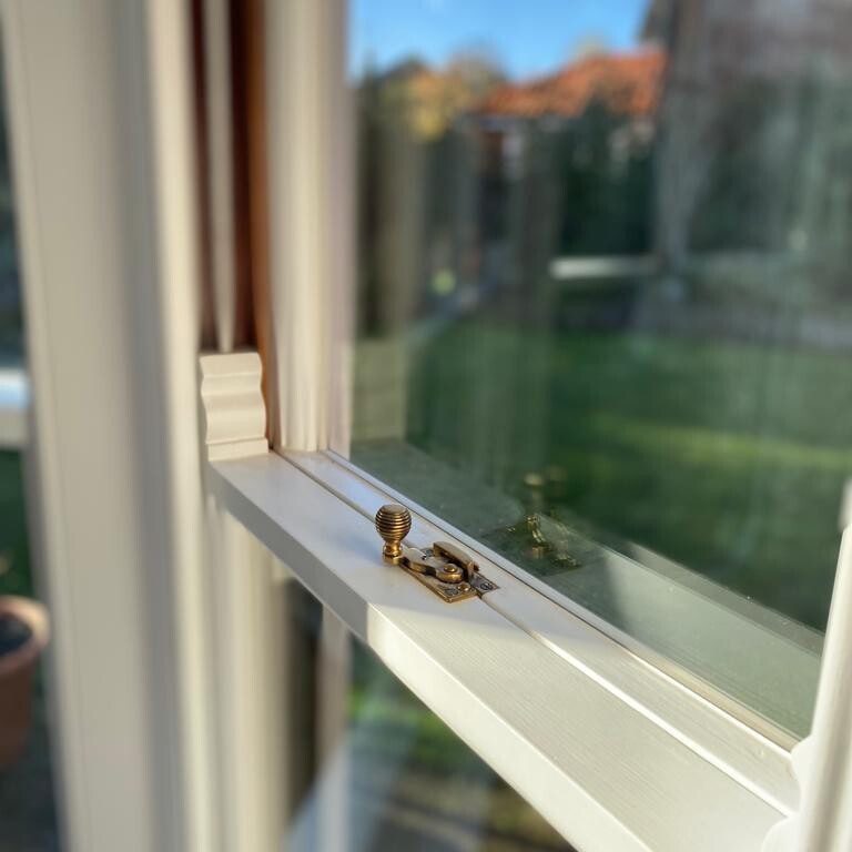 An olive green bird is perched on a window sill in Suffolk.