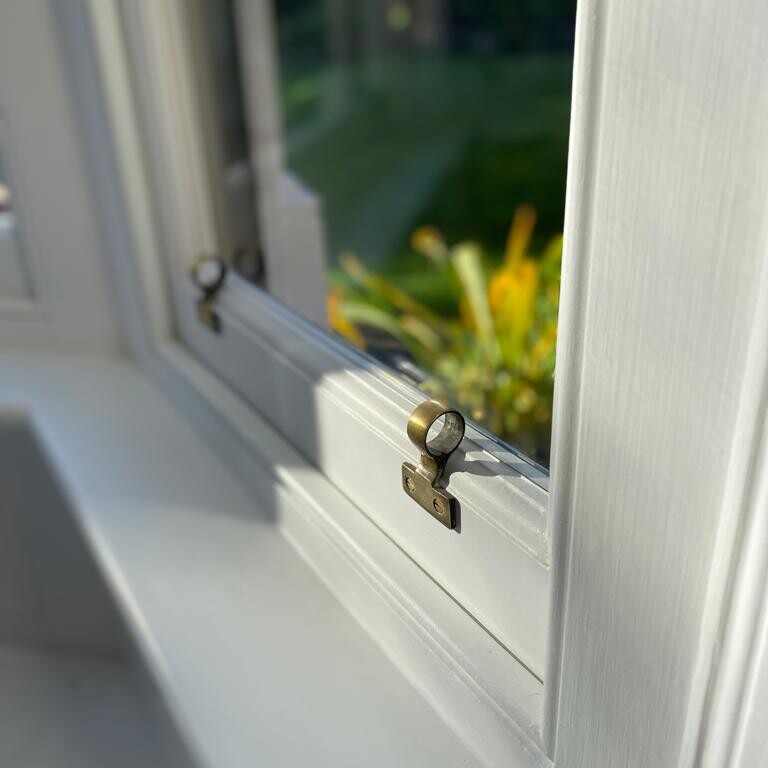 A close up of a custom white window with brass handles in Suffolk.