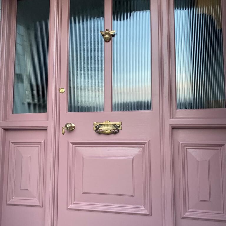 A Suffolk pink front door with a brass handle.