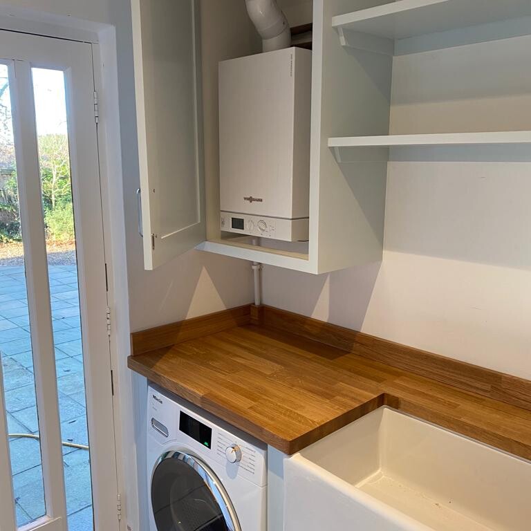 A laundry room with custom olive green joinery and a washing machine.